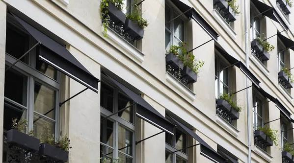 Stone hotel frontage with tall shuttered windows on a narrow Paris street
