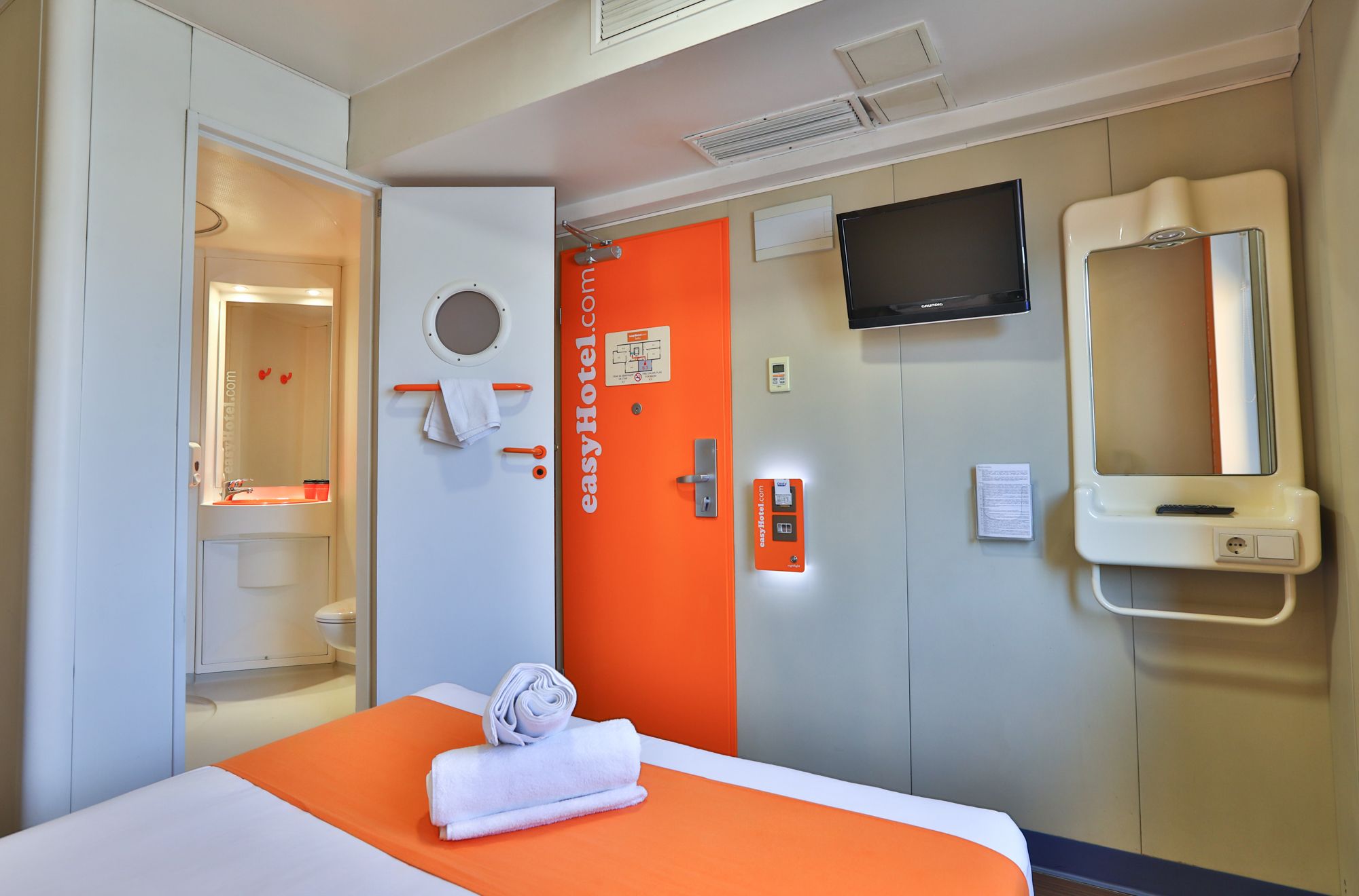 Small uniform hotel room with a bed and a compact shower unit